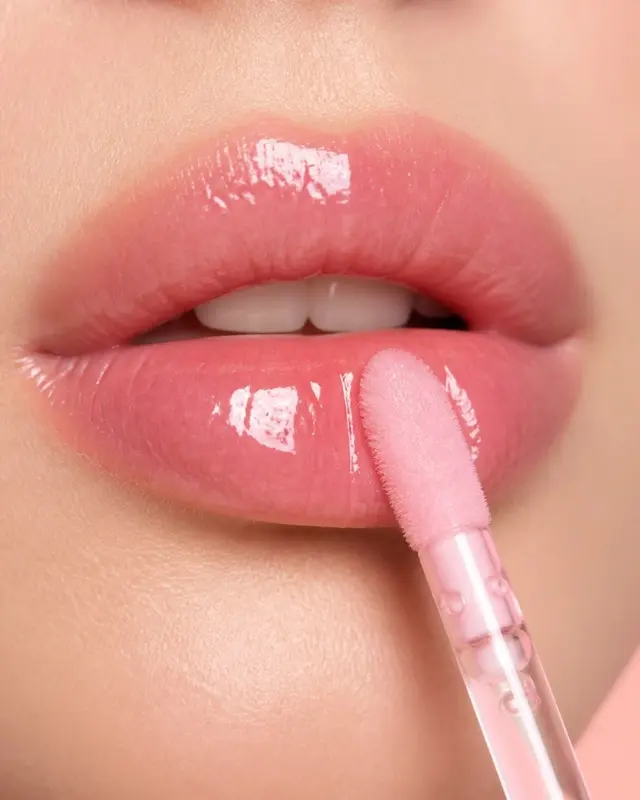 Primer plano de unos labios rosados con gloss brillante y su aplicador rosa