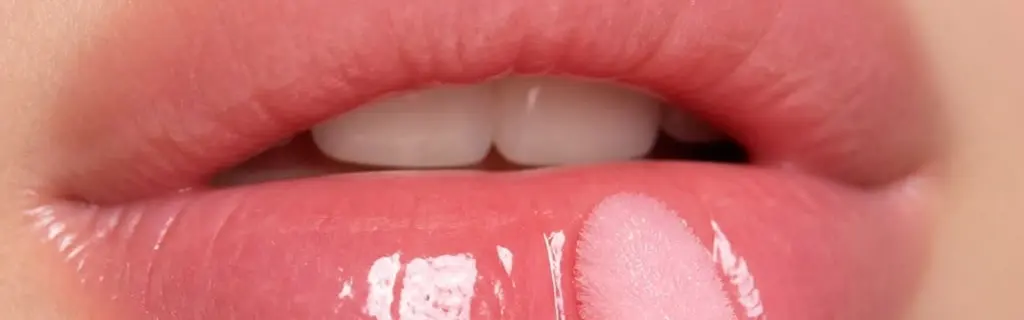 Primer plano de unos labios rosados con gloss brillante y su aplicador rosa