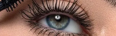 Primer plano de un ojo claro con pestañas largas y definidas mientras se aplica máscara de pestañas