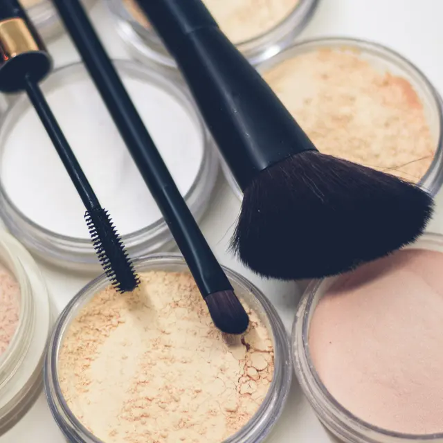 Polvos sueltos en tonos de piel claros y medios, abiertos, con brochas de maquillaje encima