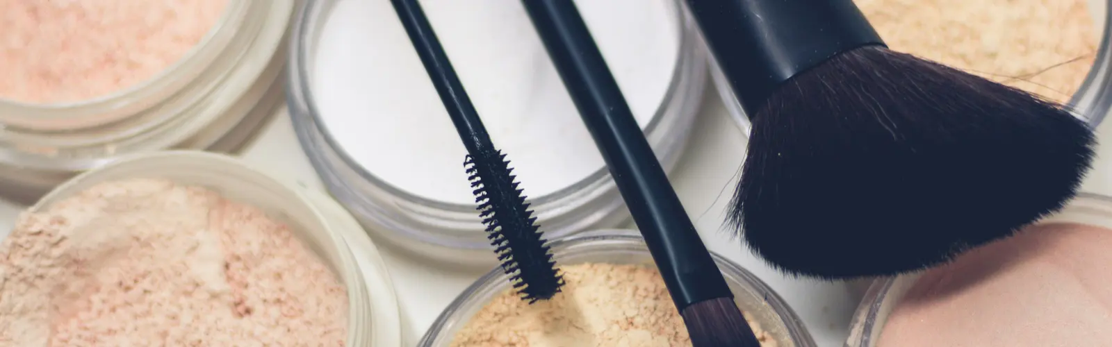 Polvos sueltos en tonos de piel claros y medios, abiertos, con brochas de maquillaje encima